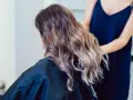Fryzjerka układa falowane włosy w odcieniu brudny blond, tworząc subtelne refleksy.