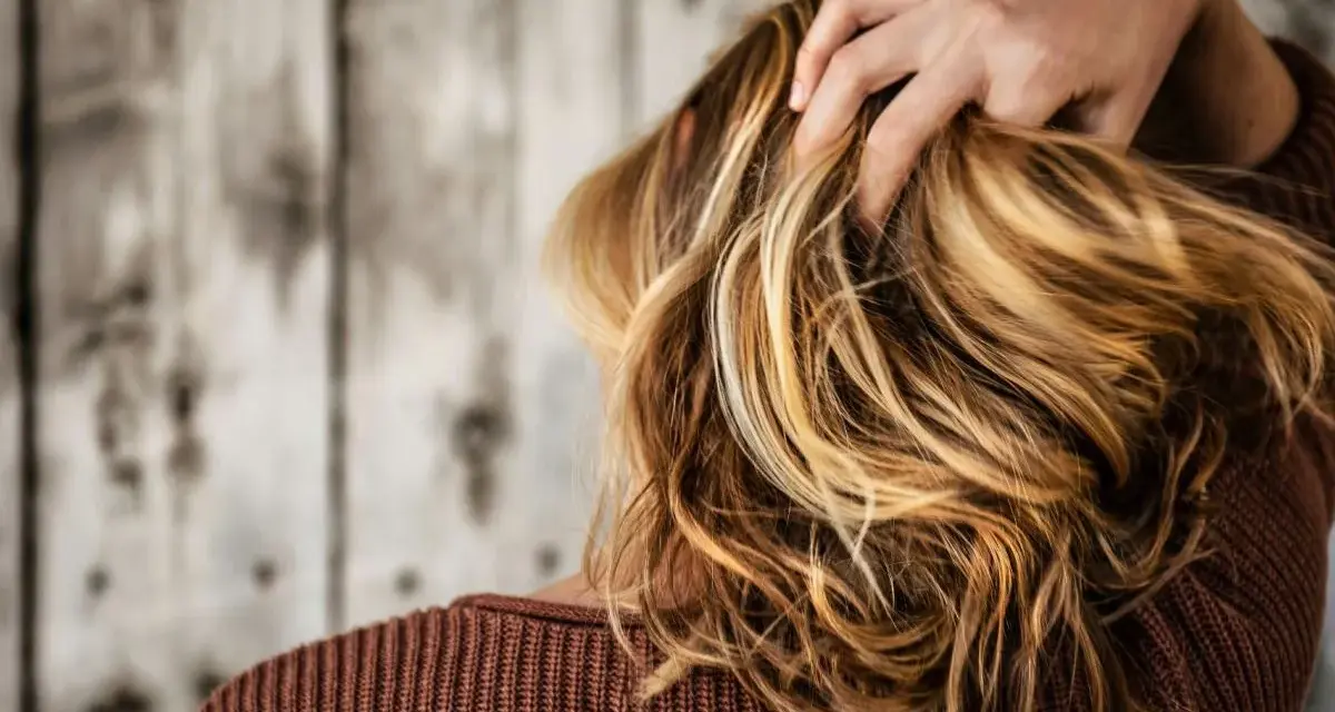 Kobieta z burzą blond włosów, które dodają jej uroku. Zastanawiasz się, jaki kolor włosów odmładza po 40? Jasne refleksy mogą zdziałać cuda!