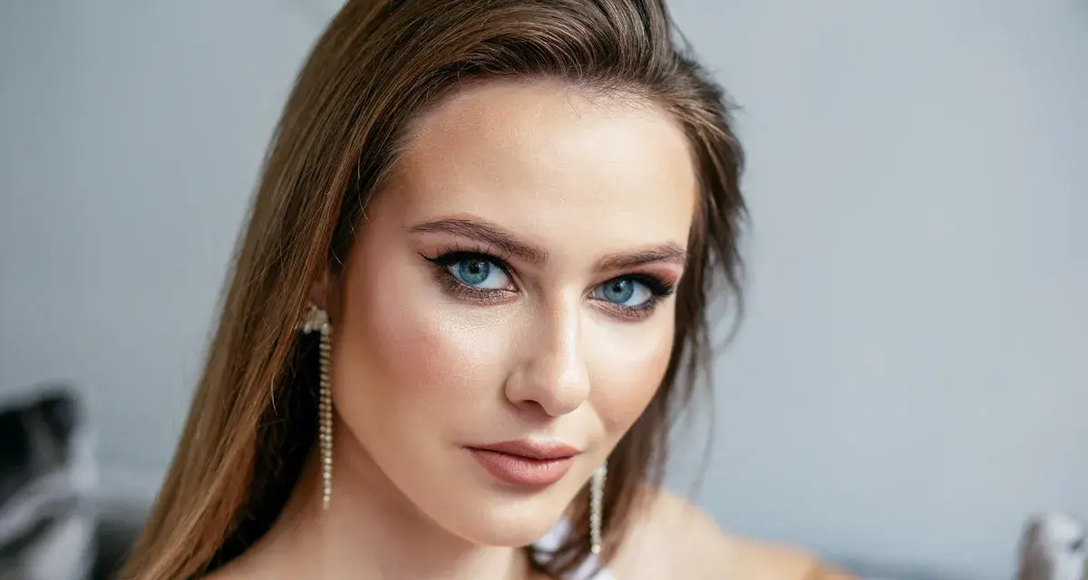 Brązowe włosy pięknie podkreślają niebieskie oczy. Modelka ma delikatny makijaż i długie, błyszczące kolczyki.