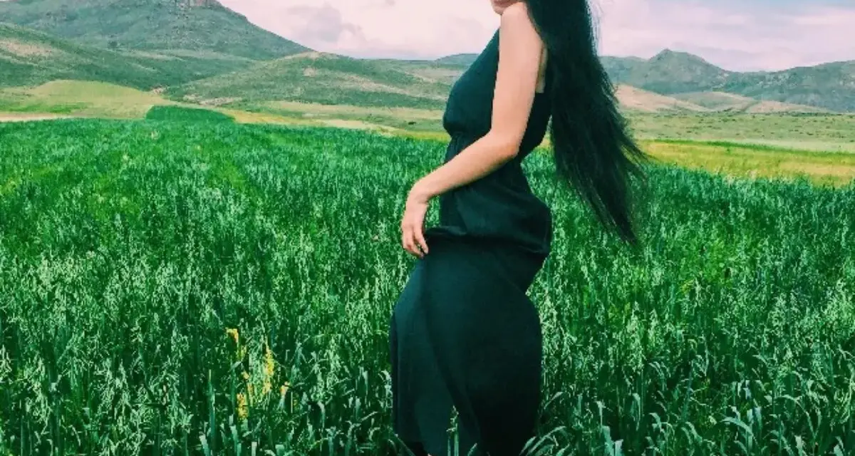 Kobieta w czarnej sukience na tle zielonego pola i gór. Czerń świetnie komponuje się z zielenią, tworząc elegancki kontrast.