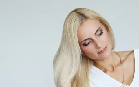 Blondynka z rozjaśniającą kąpielą włosów, delikatny makijaż oczu, złoty naszyjnik.