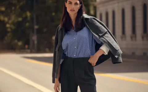 Elegancka kobieta w granatowej koszuli w paski i grafitowych spodniach. Szara marynarka narzucona na ramiona. Zastanawiasz się, jaki kolor pasuje do granatu? Oto inspiracja.