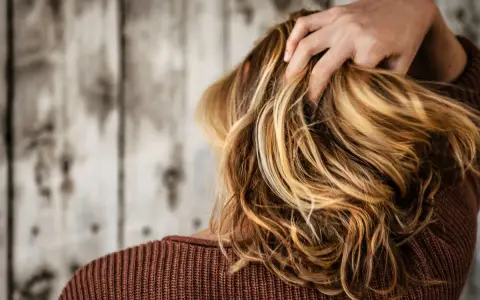 Kobieta z burzą blond włosów, które dodają jej uroku. Zastanawiasz się, jaki kolor włosów odmładza po 40? Jasne refleksy mogą zdziałać cuda!