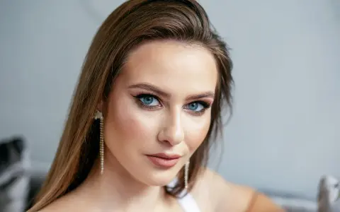 Brązowe włosy pięknie podkreślają niebieskie oczy. Modelka ma delikatny makijaż i długie, błyszczące kolczyki.