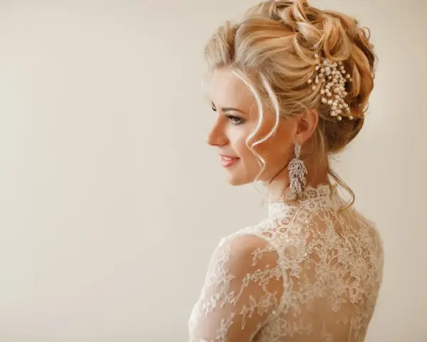 Elegancka fryzura wieczorowa z perłami i kryształowymi kolczykami. Delikatne loki opadają na ramiona.