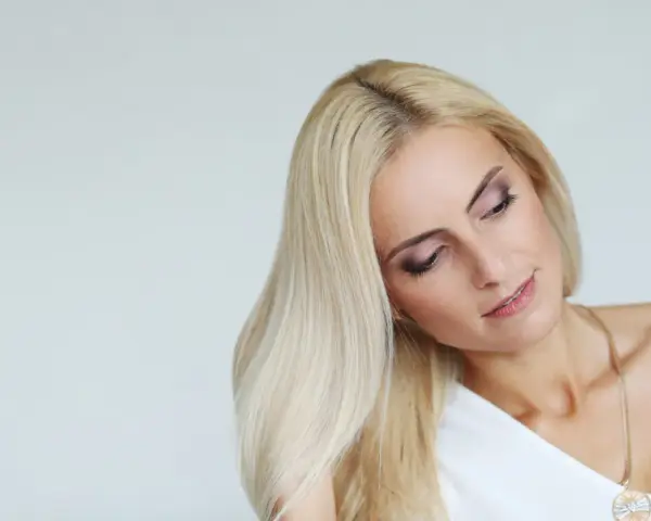 Blondynka z rozjaśniającą kąpielą włosów, delikatny makijaż oczu, złoty naszyjnik.