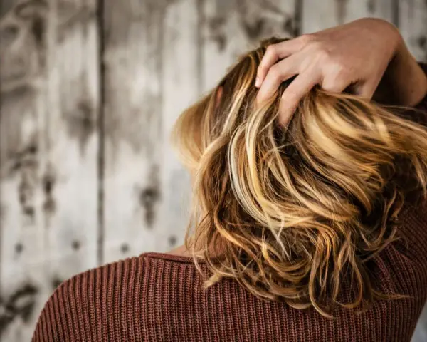 Kobieta z burzą blond włosów, które dodają jej uroku. Zastanawiasz się, jaki kolor włosów odmładza po 40? Jasne refleksy mogą zdziałać cuda!