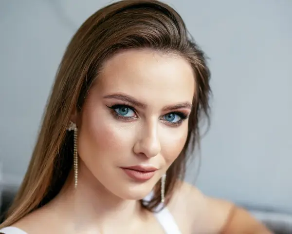 Brązowe włosy pięknie podkreślają niebieskie oczy. Modelka ma delikatny makijaż i długie, błyszczące kolczyki.