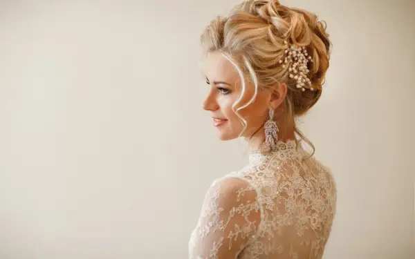 Elegancka fryzura wieczorowa z perłami i kryształowymi kolczykami. Delikatne loki opadają na ramiona.